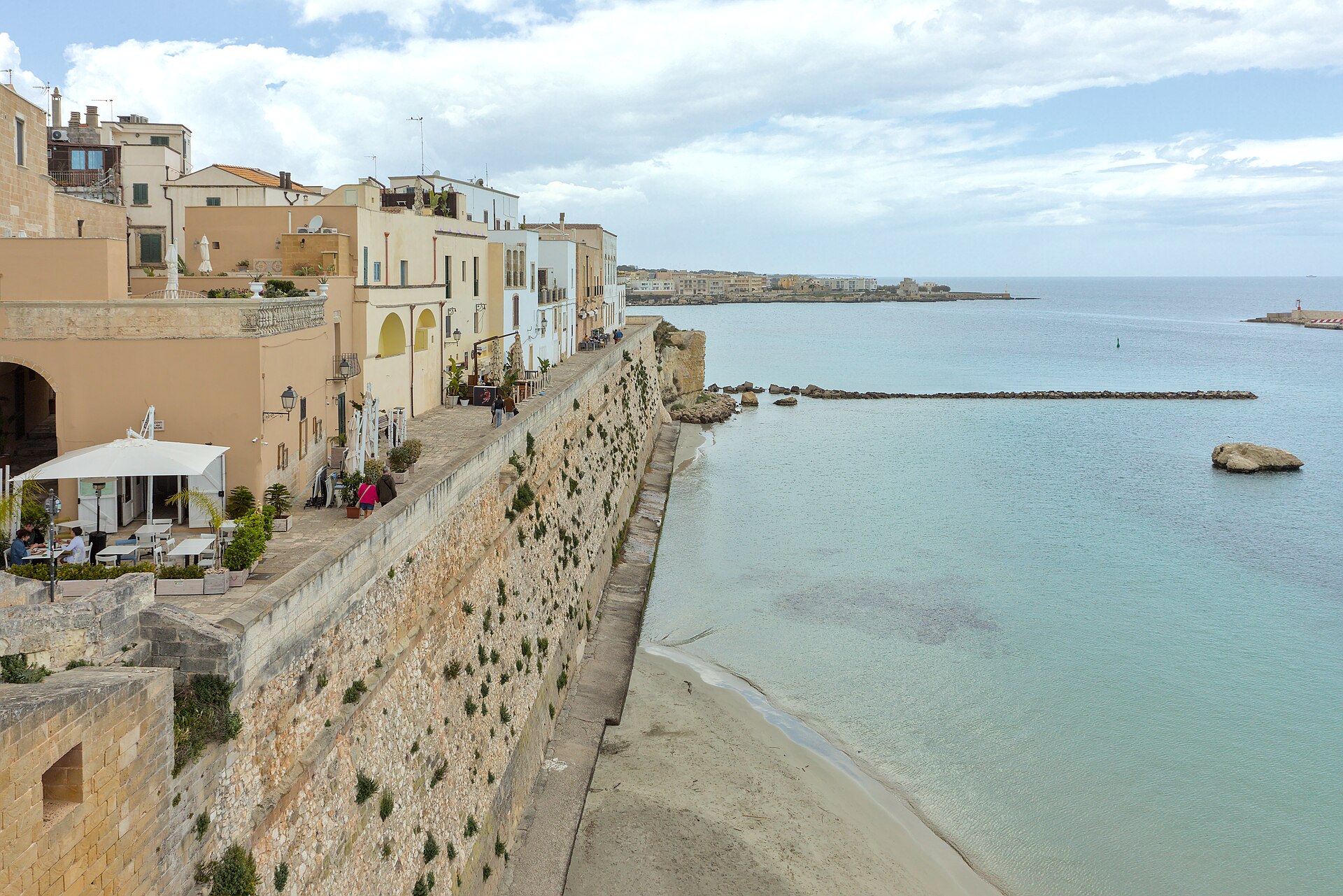 The old town walls of Otranto above a pale sandy bay